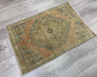Puede incluir: Una alfombra rectangular que presenta un medallón octogonal central en tonos verde oliva y marrón. La alfombra muestra un fondo naranja descolorido con intrincados patrones geométricos en los bordes y flecos cortos en los lados.
