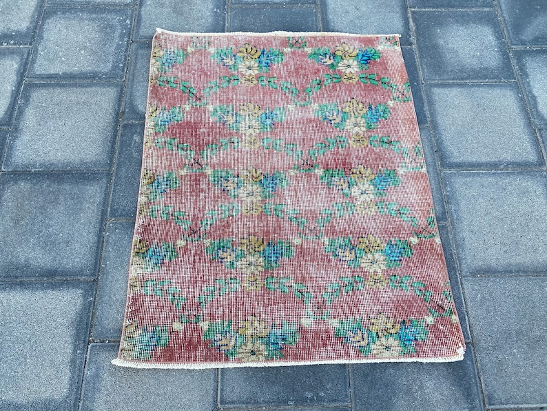 May include: A vintage floral patterned rug with a red background and green vines. The rug has a white fringe border.