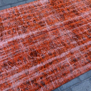 May include: A distressed rug with a faded orange and black pattern. The rug has a worn and vintage look.