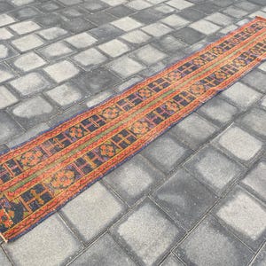 May include: A long, narrow rug with a traditional Persian design. The rug has a dark blue background with red, orange, and yellow accents. The rug is made of wool and has a hand-knotted texture.