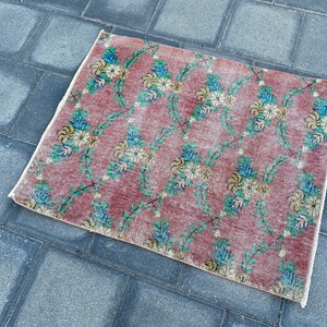 May include: A vintage floral patterned rug with a pink background and green vines. The rug has a faded look and is made of a soft, woven material.