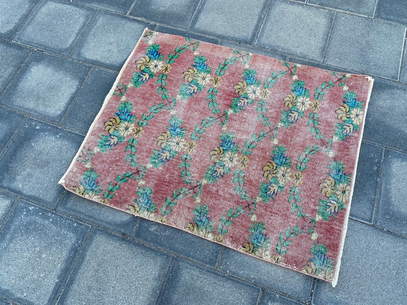 May include: A vintage floral patterned rug with a pink background and green vines. The rug has a faded look and is made of a soft, woven material.