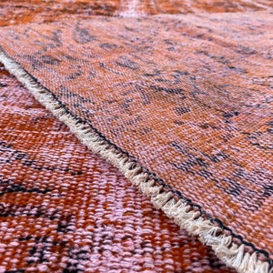 May include: Close-up of a woven rug with a fringe border. The rug has a brown and pink color scheme with a subtle pattern.