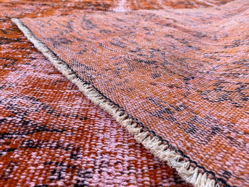 May include: Close-up of a woven rug with a fringe border. The rug has a brown and pink color scheme with a subtle pattern.