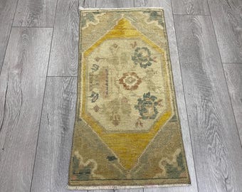 Puede incluir: Alfombra rectangular anudada a mano con un diseño central de diamante amarillo. La alfombra presenta motivos florales en verde, azul y naranja sobre un fondo beige. El borde es verde apagado con flecos beige.