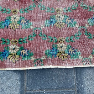 May include: A vintage rug with a floral pattern in shades of red, green, yellow, and blue. The rug has a fringed edge and is made of a woven material.