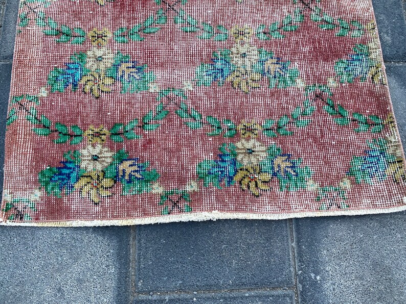 May include: A vintage rug with a floral pattern in shades of red, green, yellow, and blue. The rug has a fringed edge and is made of a woven material.