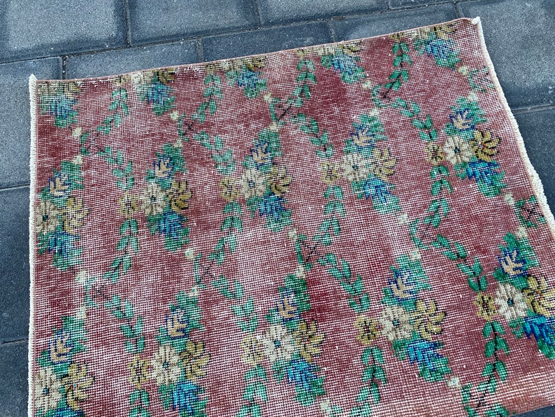 May include: A vintage rug with a floral pattern in shades of pink, green, yellow, and blue. The rug has a distressed look and is made of a woven material.
