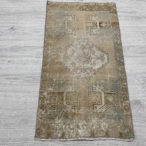 May include: A rectangular area rug featuring a faded, distressed pattern in shades of beige, brown, and muted blue. The design includes a central geometric medallion surrounded by intricate, angular motifs and a bordered edge with fringe.