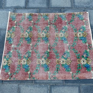May include: A vintage floral rug with a red background and a white border. The rug features a repeating pattern of green vines and yellow and blue flowers.
