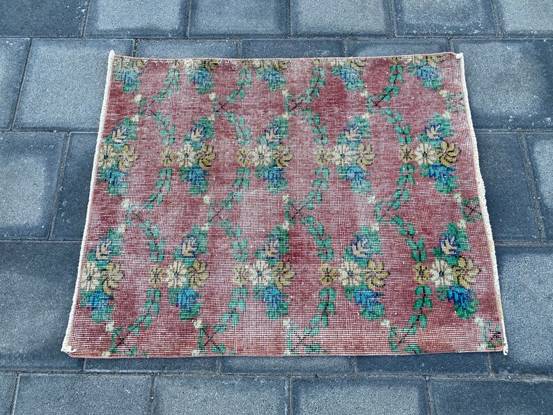 May include: A vintage floral rug with a red background and a white border. The rug features a repeating pattern of green vines and yellow and blue flowers.