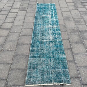 May include: A teal blue runner rug with a faded, distressed look. The rug has a subtle pattern and is made of a soft, woven material.