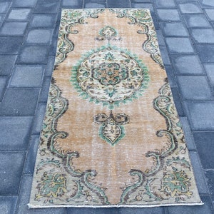 May include: A vintage style runner rug with a beige background and a green and brown floral pattern. The rug has a distressed look and is perfect for adding a touch of bohemian style to your home.