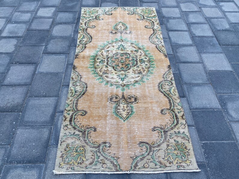 May include: A vintage style runner rug with a beige background and a green and brown floral pattern. The rug has a distressed look and is perfect for adding a touch of bohemian style to your home.
