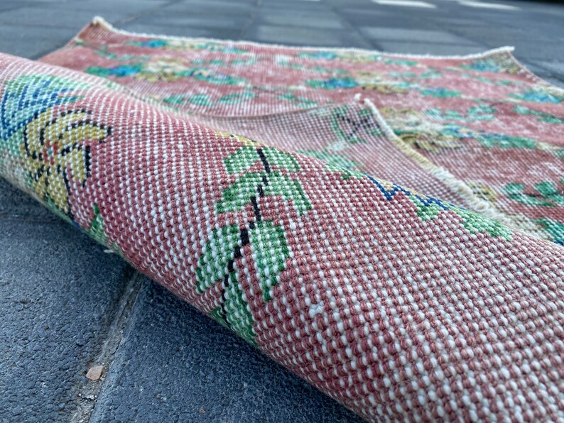 May include: A close-up of a pink and white woven rug with a floral pattern. The rug is rolled up and the floral pattern is visible on the outside of the roll.