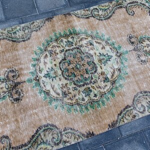 May include: A vintage rug with a faded beige background and intricate green and brown floral patterns. The rug has a distressed look and is perfect for adding a touch of bohemian style to any room.
