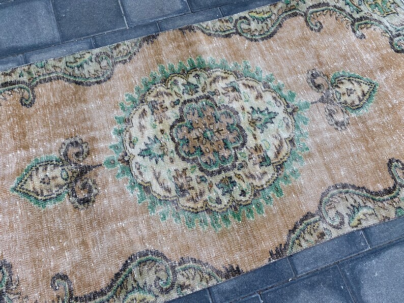 May include: A vintage rug with a faded beige background and intricate green and brown floral patterns. The rug has a distressed look and is perfect for adding a touch of bohemian style to any room.