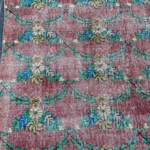 May include: A vintage rug with a floral pattern in shades of pink, green, blue, and yellow. The rug has a distressed look and is made of a woven material.