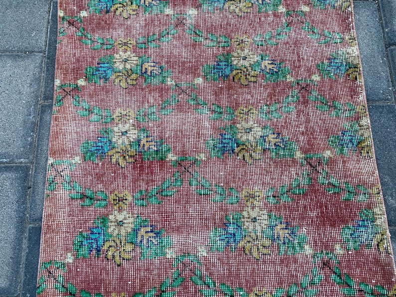 May include: A vintage rug with a floral pattern in shades of pink, green, blue, and yellow. The rug has a distressed look and is made of a woven material.