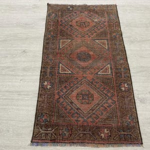 May include: A rectangular woven rug featuring a dark brown background with a series of three large, centered diamond motifs in shades of terracotta, rust, and muted blue. The border displays geometric patterns with small floral accents.