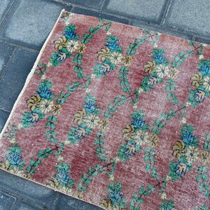May include: A vintage rug with a floral pattern in shades of pink, green, blue, and yellow. The rug has a distressed look and is made of a soft, woven material.
