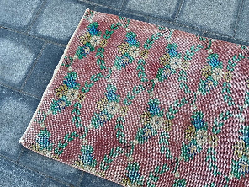 May include: A vintage rug with a floral pattern in shades of pink, green, blue, and yellow. The rug has a distressed look and is made of a soft, woven material.