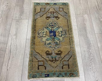 Puede incluir: Una alfombra rectangular de estilo vintage con un diseño geométrico central. La alfombra presenta un fondo beige con detalles en azul, turquesa y gris. El borde es turquesa. Las dimensiones de la alfombra no son visibles.