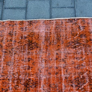 May include: A vintage rug with a faded orange and brown color scheme. The rug has a distressed look with a floral pattern.