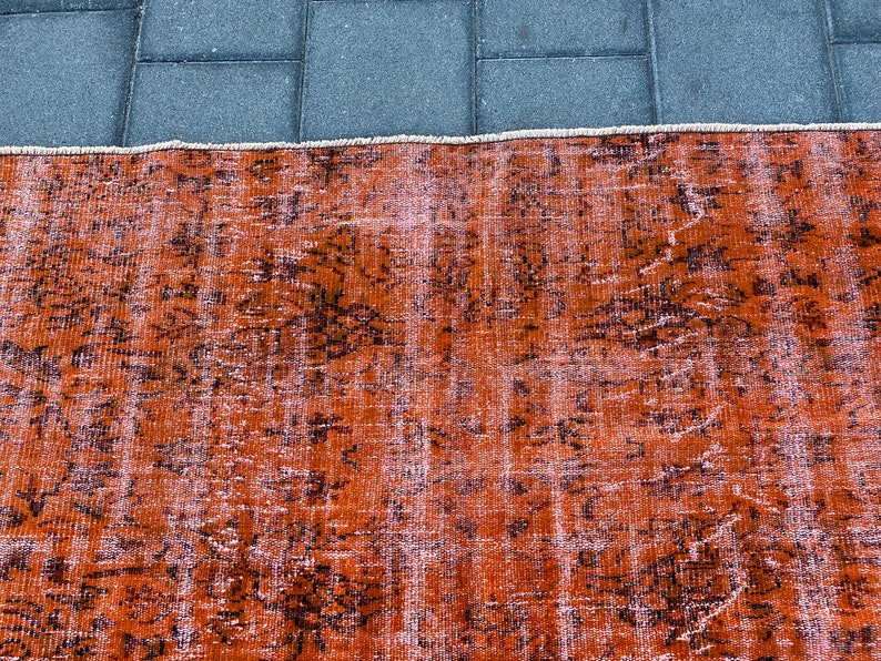 May include: A vintage rug with a faded orange and brown color scheme. The rug has a distressed look with a floral pattern.