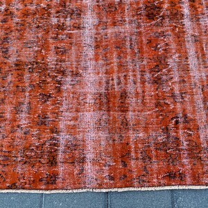 May include: A vintage-style rug with a distressed, faded look. The rug is a deep orange color with a black and white pattern. The rug has a fringe border.
