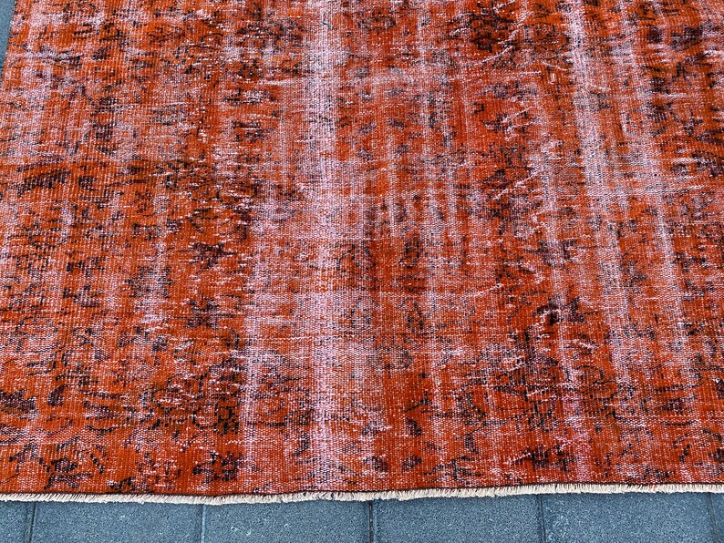 May include: A vintage-style rug with a distressed, faded look. The rug is a deep orange color with a black and white pattern. The rug has a fringe border.