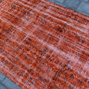 May include: A vintage distressed rug with a faded orange and black pattern. The rug has a worn and textured look, giving it a rustic and antique feel.