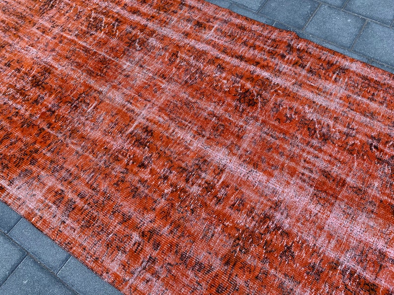 May include: A vintage distressed rug with a faded orange and black pattern. The rug has a worn and textured look, giving it a rustic and antique feel.