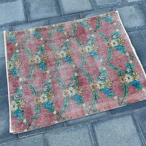 May include: A vintage floral patterned rug with a pink background and a faded look. The rug has a floral design with green leaves and yellow, blue, and white flowers.