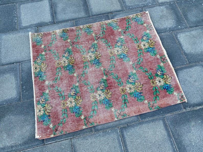 May include: A vintage floral patterned rug with a pink background and a faded look. The rug has a floral design with green leaves and yellow, blue, and white flowers.