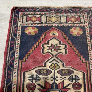 Puede incluir: Una alfombra tejida rectangular que presenta un campo central azul marino profundo con un gran dise&ntilde;o de mihrab en forma de escalones de color rosa oscuro. La alfombra est&aacute; decorada con motivos florales geom&eacute;tricos en crema, amarillo y rojo oscuro.