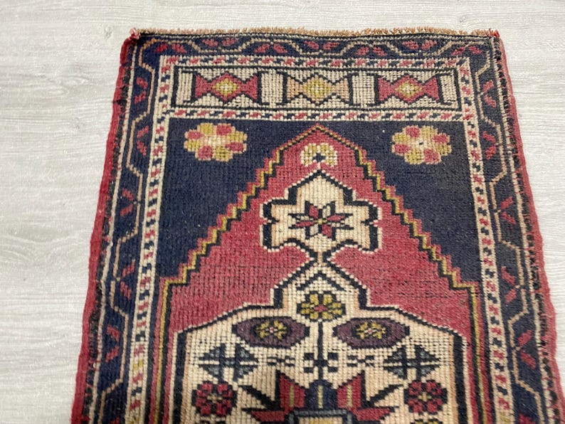 Puede incluir: Una alfombra tejida rectangular que presenta un campo central azul marino profundo con un gran dise&ntilde;o de mihrab en forma de escalones de color rosa oscuro. La alfombra est&aacute; decorada con motivos florales geom&eacute;tricos en crema, amarillo y rojo oscuro.