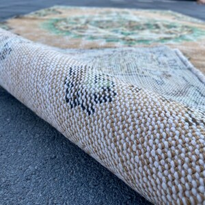 May include: Close-up of a rolled-up rug with a beige and white woven pattern. The rug has a subtle green and brown design.