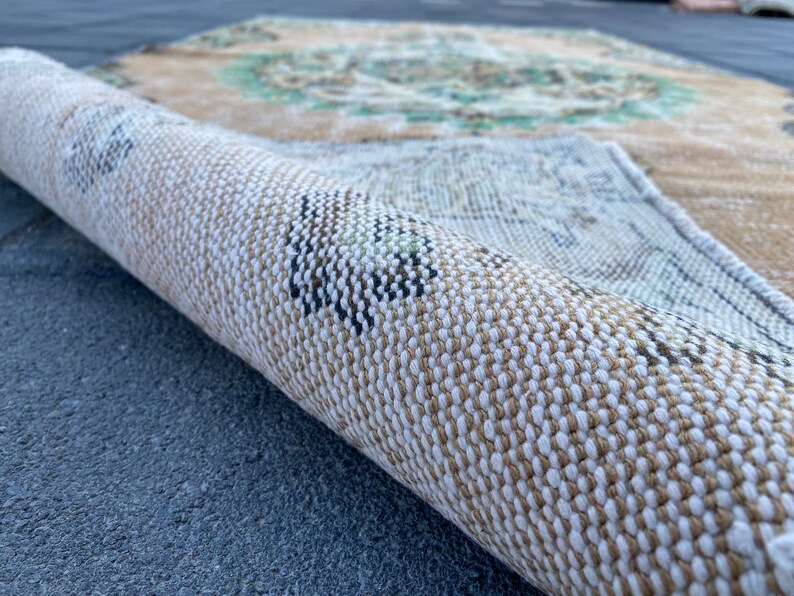 May include: Close-up of a rolled-up rug with a beige and white woven pattern. The rug has a subtle green and brown design.