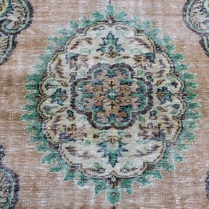 May include: A vintage rug with a beige background and a large, intricate green, brown, and white floral design in the center.