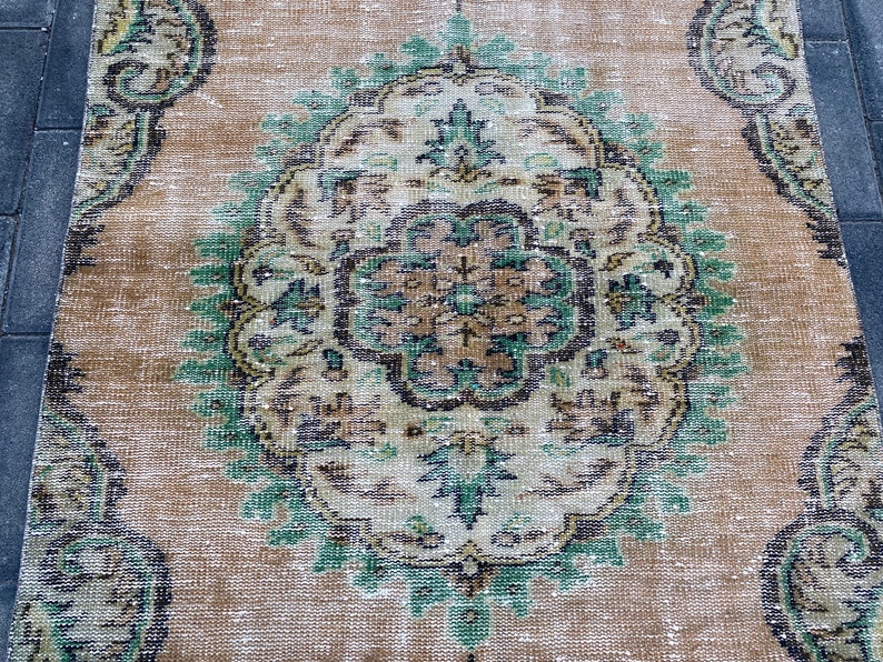 May include: A vintage rug with a beige background and a large, intricate green, brown, and white floral design in the center.