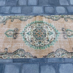 May include: A vintage rug with a beige background and a green and brown floral pattern. The rug has a distressed look and is perfect for adding a touch of bohemian style to your home.