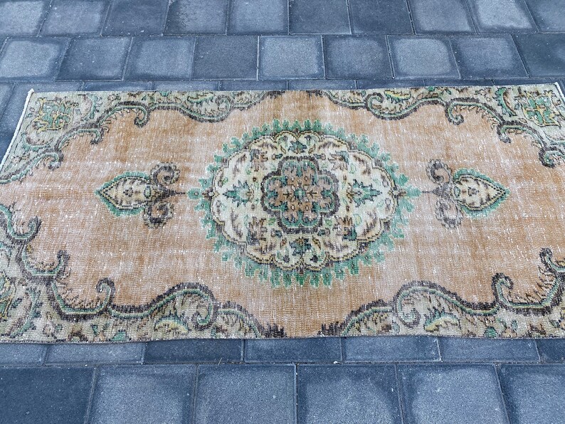 May include: A vintage rug with a beige background and a green and brown floral pattern. The rug has a distressed look and is perfect for adding a touch of bohemian style to your home.