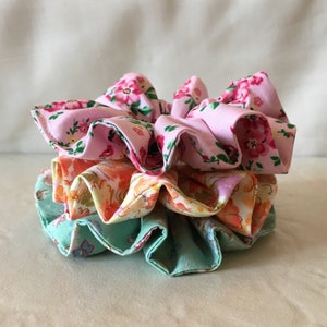 May include: A stack of three fabric scrunchies in pink, orange, and green with floral patterns.