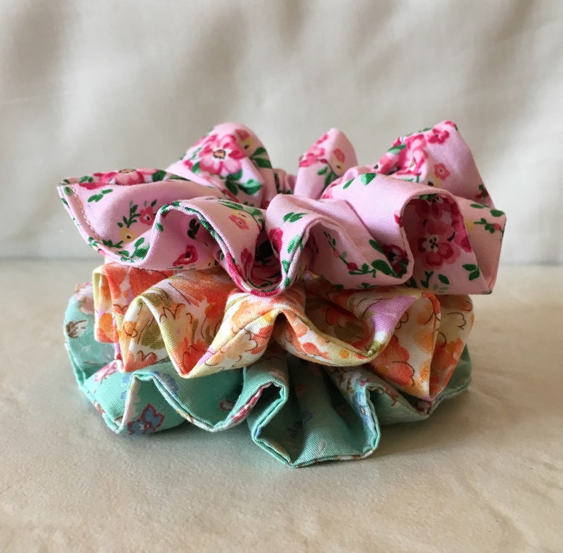 May include: A stack of three fabric scrunchies in pink, orange, and green with floral patterns.