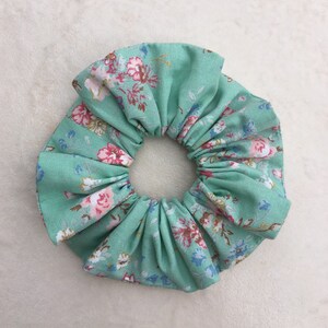 May include: A green fabric scrunchie with a floral pattern. The scrunchie is made of a soft, stretchy fabric and is perfect for holding hair in place.