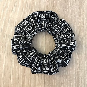 May include: Black and white scrunchie with a periodic table pattern. The scrunchie is made of fabric and has a gathered design.