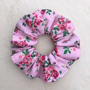 May include: A pink scrunchie with a floral pattern. The scrunchie is made of fabric and has a gathered design.