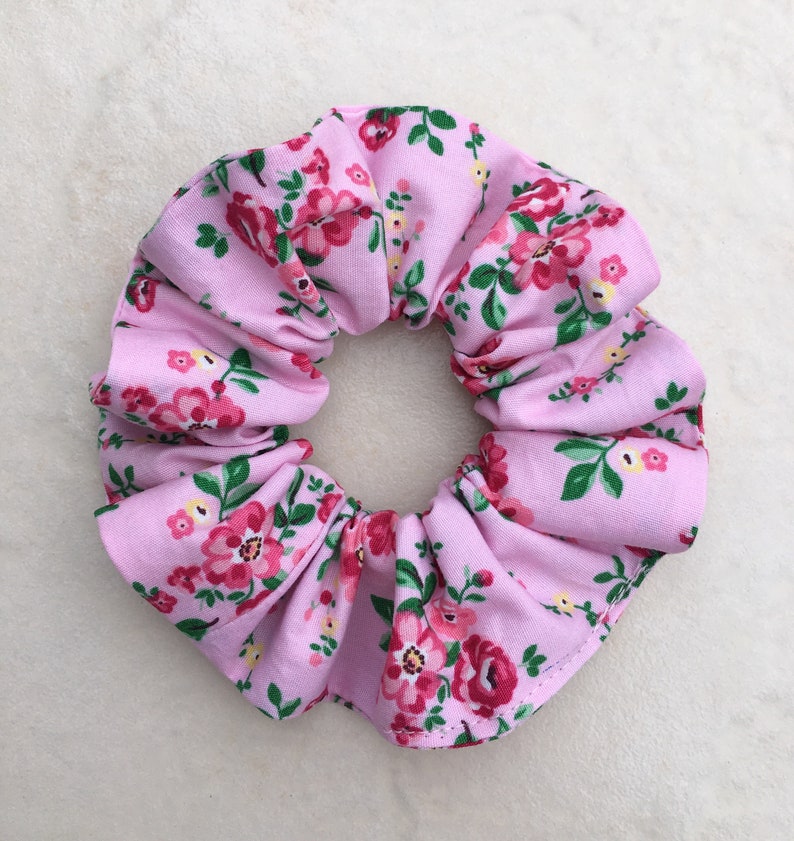 May include: A pink scrunchie with a floral pattern. The scrunchie is made of fabric and has a gathered design.