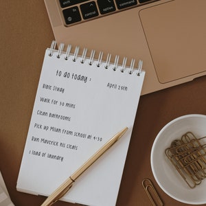 May include: A white notebook with a gold spiral binding and a to-do list for April 25th. The list includes items like "Bible Study", "Walk for 30 mins", "Clean bathrooms", "Pick up Milan from school at 4:30", "Run Maverick his cleats", and "1 load of laundry".